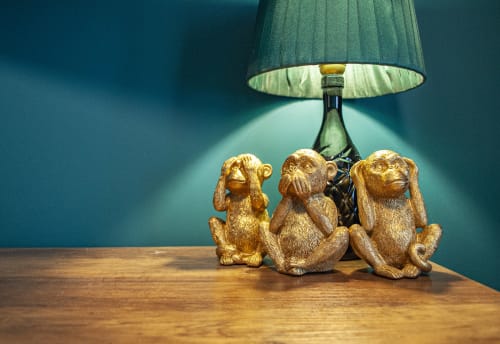 Three golden monkey figurines under a green lamp on wooden table in Vesuvio's Room at LH51 Napoli