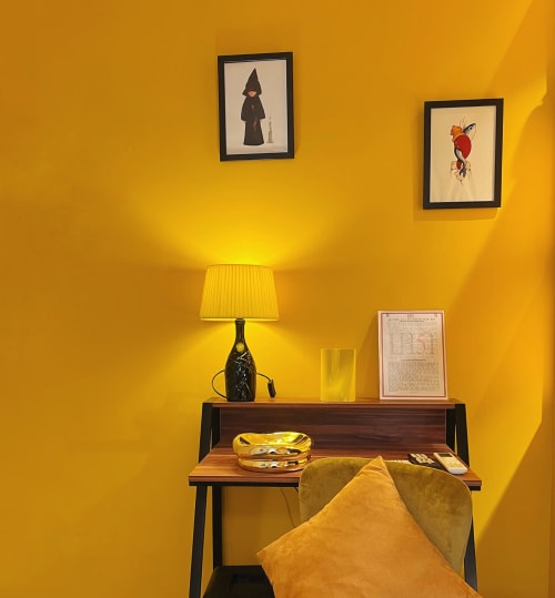 Stanza gialla luminosa a LH51 Napoli con scrivania, lampada, opera d'arte incorniciata e cuscino color senape