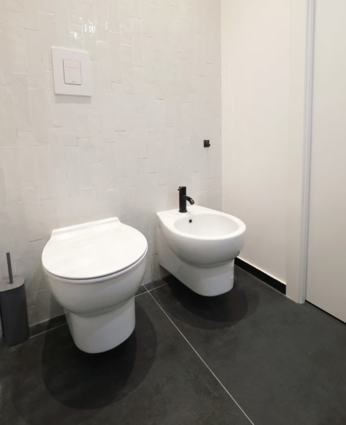 Bagno moderno alle LH51 Rooms di Napoli con toilette e bidet bianchi, pavimento scuro e pareti piastrellate