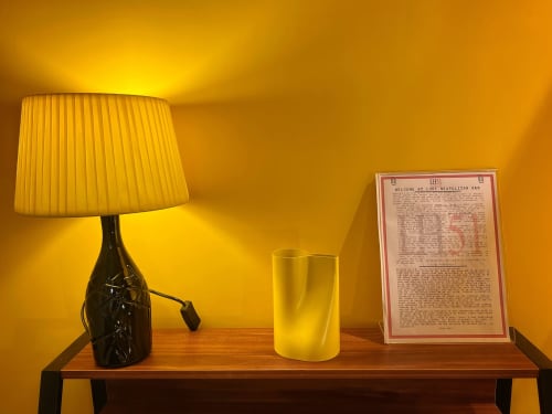 Ripiano illuminato in caldo giallo presso LH51 Naples B&B con lampada da tavolo, candela gialla e cartello di benvenuto
