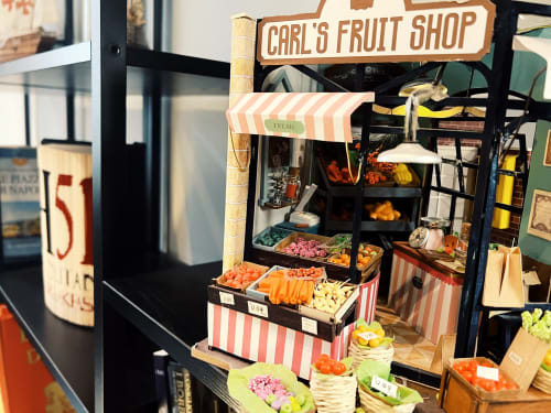 Carl's Fruit Shop miniature display at LH51 Rooms in Naples featuring produce and striped awning