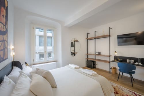 Camera moderna a Palazzo Garibaldi Parma con letto bianco, scaffalature in legno, scrivania e vista sulla città dalle ampie finestre