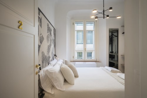 Chambre lumineuse et contemporaine au Palazzo Garibaldi Parma avec literie blanche, grande fenêtre et luminaires suspendus design
