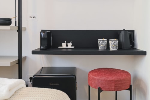 Étagère moderne dans une chambre d'hôtel du Palazzo Garibaldi Parma avec cafetière, tasses et tabouret ottoman rouge