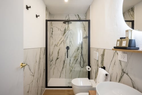 Salle de bain moderne du Palazzo Garibaldi Parma avec douche en marbre, sanitaires blancs et détails en bois