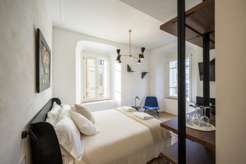 Chambre moderne au Palazzo Garibaldi Parma avec lit queen-size, fauteuil bleu, luminaires suspendus et grandes fenêtres dominant la