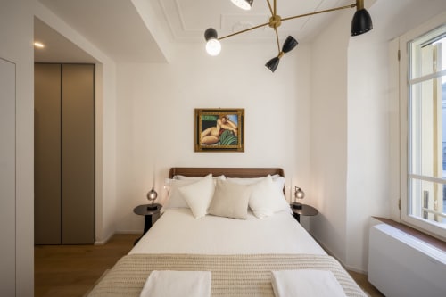 Chambre moderne au Palazzo Garibaldi Parma avec literie blanche, tête de lit en bois, luminaires suspendus et œuvres encadrées
