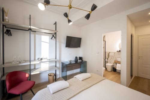 Chambre moderne du Palazzo Garibaldi Parma avec lit, fauteuil rouge, bureau, TV et salle de bains attenante