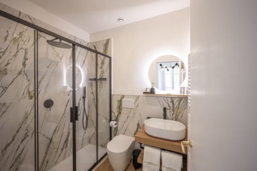Salle de bains moderne au Palazzo Garibaldi Parma avec carrelage marbre, douche à effet pluie, vasque et miroir rétroéclairé