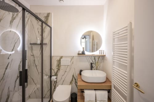 Salle de bain moderne au Palazzo Garibaldi Parma avec carrelage en marbre, miroir rond lumineux, vasque blanche et douche cascade