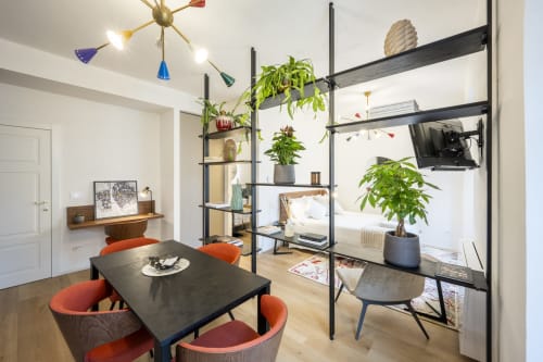 Studio moderne au Palazzo Garibaldi Parma avec table à manger noire, chaises orange, étagères avec plantes et coin chambre