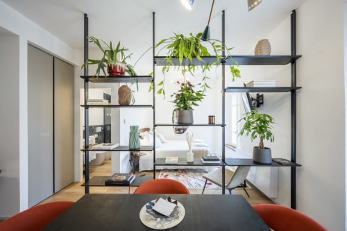 Chambre d'hôtel moderne au Palazzo Garibaldi Parma avec étagères noires, plantes suspendues, table à manger et chaises oranges
