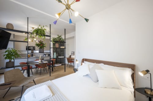 Chambre d'hôtel moderne au Palazzo Garibaldi Parma avec lit, bureau, luminaire coloré, plantes et séjour ouvert