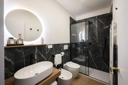 Salle de bain moderne au Palazzo Garibaldi Parma avec murs en marbre noir, baignoire autoportante blanche et douche à effet pluie.