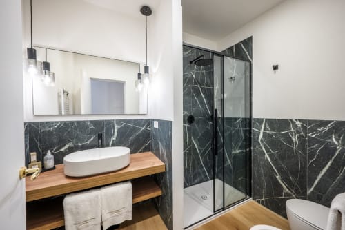 Salle de bain moderne au Palazzo Garibaldi Parma avec murs en marbre noir, meuble de salle de bain en bois, lavabo ovale et douche vitrée