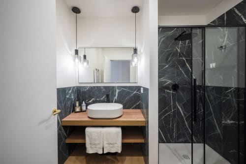 Salle de bain moderne au Palazzo Garibaldi Parma avec murs en marbre noir, meuble vasque en bois, lavabo rond et douche vitrée