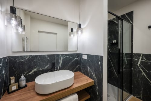 Salle de bain moderne au Palazzo Garibaldi Parma avec mur en marbre, vasque blanche ovale, meuble en bois, luminaires suspendus et douche vitrée
