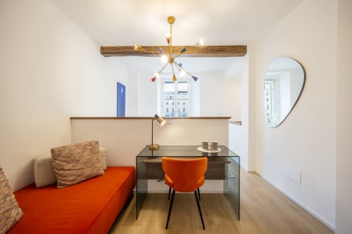Chambre d'hôtel moderne au Palazzo Garibaldi Parma avec lit orange, bureau en verre, lustre en laiton et vue sur la ville