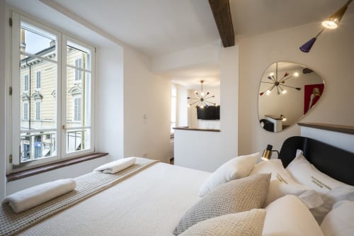 Chambre d'hôtel moderne au Palazzo Garibaldi Parma avec literie blanche, miroir arqué et vue sur la ville par grandes fenêtres