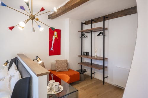 Chambre d'hôtel moderne au Palazzo Garibaldi Parma avec poutres en bois, ottoman orange, étagères et luminaire suspendu coloré