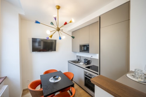 Chambre moderne du Palazzo Garibaldi Parma avec fauteuils orange, kitchenette, TV murale et luminaire au plafond coloré