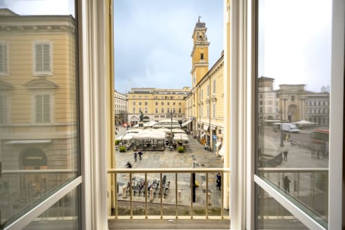 Vue depuis une chambre du Palazzo Garibaldi à Parme surplombant la piazza historique avec son clocher jaune et les parasols de la terrasse