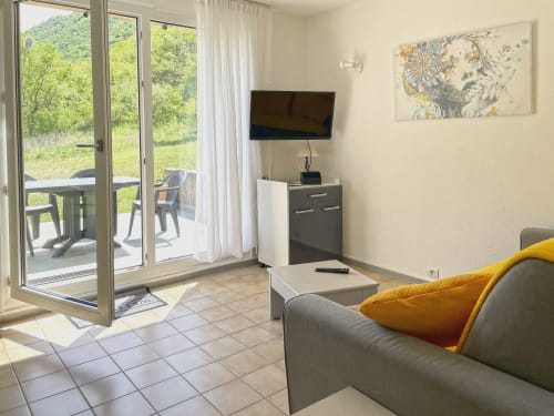 Salon moderne avec canapé gris, vue montagne, terrasse, TV et coussin terracotta chez LOCADIGNE Digne-les-Bains