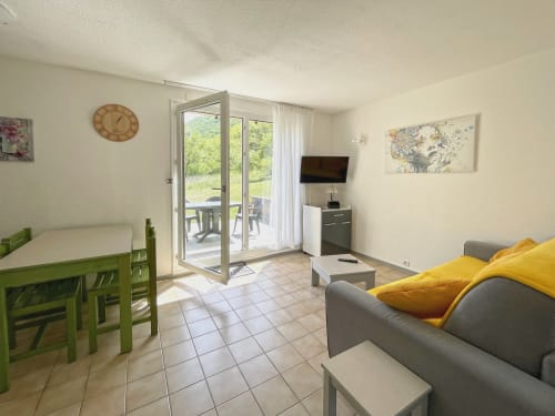 Séjour lumineux LOCADIGNE Digne-les-Bains : canapé gris, table de salle à manger verte, TV et accès terrasse