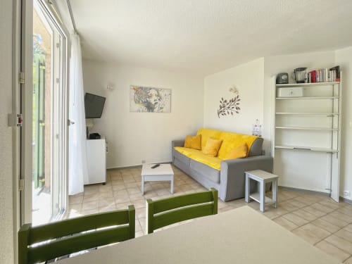 Séjour lumineux à LOCADIGNE Digne-les-Bains avec canapé gris, coussins jaunes, TV, étagères blanches et terrasse