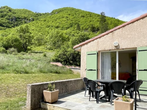 Terrasse avec chaises noires à l'appartement LOCADIGNE à Digne-les-Bains, collines verdoyantes et bâtisse en pierre aux volets