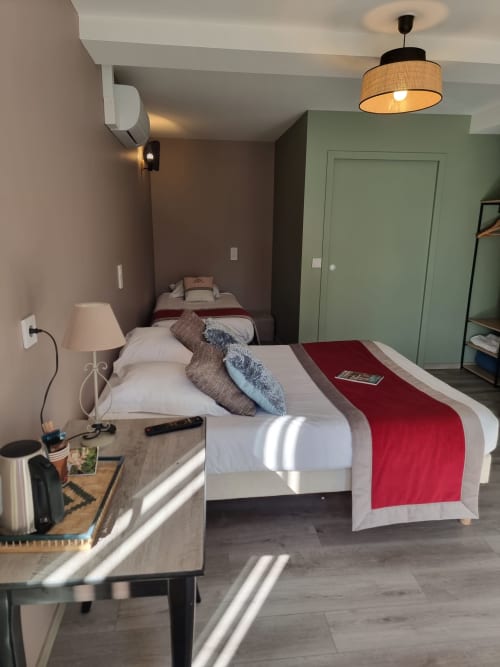 Chambre triple Hôtel Amadour à Rocamadour avec deux lits, literie rouge, bureau et équipements modernes incluant TV et climatisation