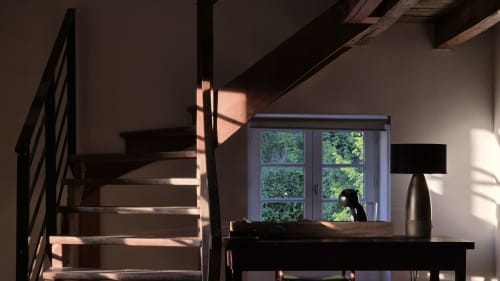 Sunlit bedroom at Moulin Renaudiots in Autun with wooden staircase, desk, and garden view through windows