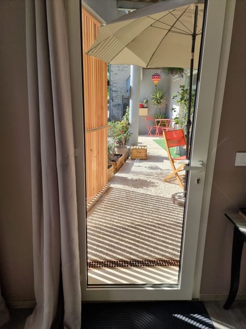 Terrasse ensoleillée de l'Hôtel Amadour à Rocamadour avec parasol, plantes et chaises rouges