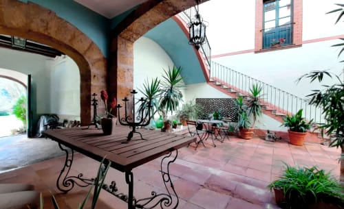 Patio del hotel Can Carol en Capellades con baldosas de terracota, columnas de ladrillo arqueado, farol colgante y plantas en macetas