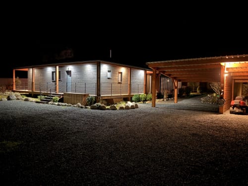 Villa moderne illuminée la nuit, cour de gravier, pergola en bois et aménagement paysager aux Villas Vallée d'Asco