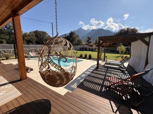 Fauteuil en osier suspendu sur terrasse en bois dominant piscine chauffée et montagnes à Villa Cinto, Moltifao Corse