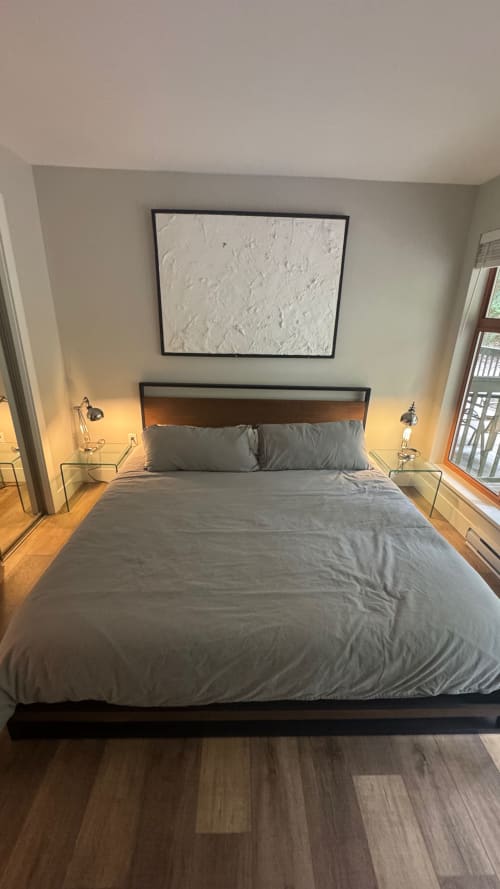 Modern bedroom in Whistler apartment with gray bedding, wood headboard, framed white abstract art, bedside lamps, hardwood