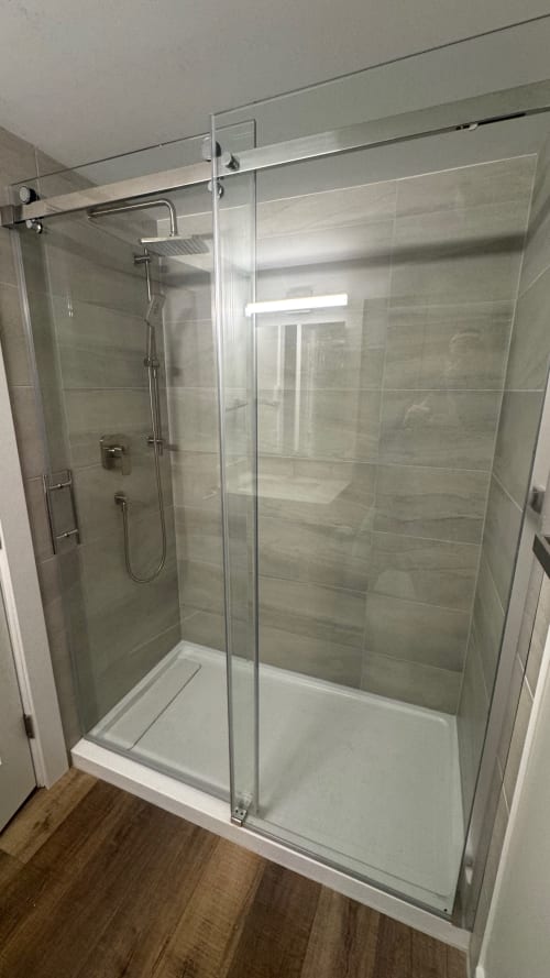 Modern glass-enclosed shower with gray tile walls and rainfall showerhead in Whistler apartment bathroom