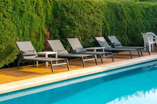 Elegantes tumbonas junto a la piscina de Guest Homes Málaga con agua turquesa y setos podados