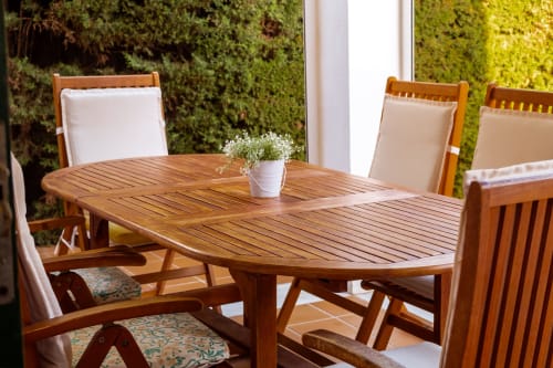 Mesa de comedor ovalada de madera con sillas tapizadas blancas y flores frescas en Guest Homes Málaga, con pared verde viviente de fondo