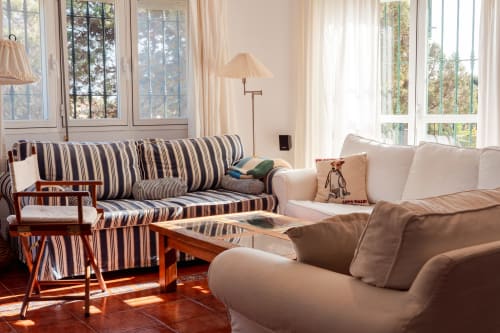 Luminoso salón con sofá rayado, sillones color crema, muebles de madera y amplias ventanas con vistas a los jardines de Guest Homes