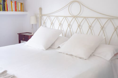 Dormitorio luminoso en Guest Homes Málaga con cabecero de metal crema, almohadas blancas y mesita de noche de madera con lámpara
