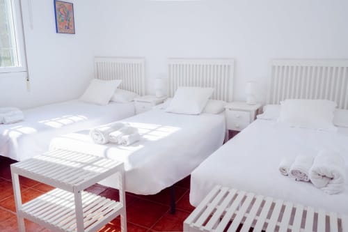 Habitación luminosa con varias camas en Guest Homes Málaga, con ropa de cama blanca, radiadores y suelo de baldosas rojas