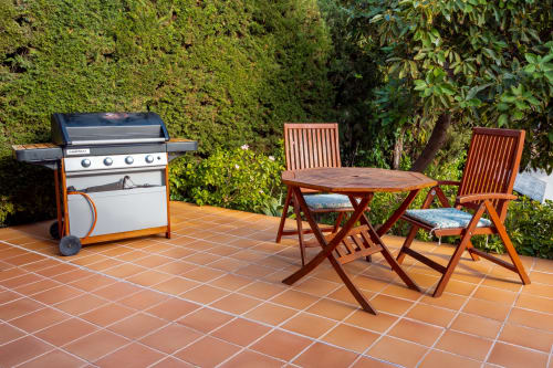 Terraza exterior de Guest Homes Málaga con parrilla, mesa de comedor y sillas de madera rodeadas de vegetación