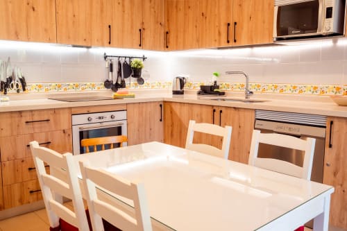 Cocina moderna en Guest Homes Málaga con muebles de madera, mesa de comedor blanca y azulejos de salpicadero con patrón amarillo.