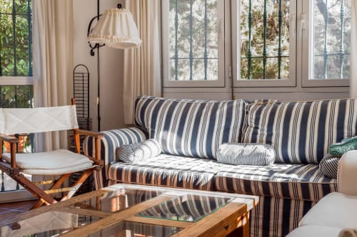 Luminoso salón con sofá a rayas, muebles de madera y ventanales que dan a los árboles en Guest Homes Málaga