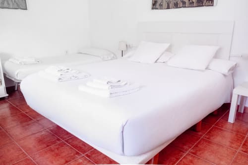 Dormitorio moderno en Guest Homes Málaga con camas blancas sobre suelo de baldosas rojas y almohadas blancas