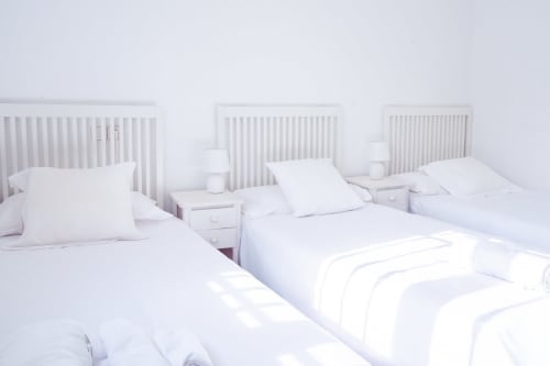 Tres camas blancas con almohadas en luminosa habitación minimalista del hotel Guest Homes Málaga