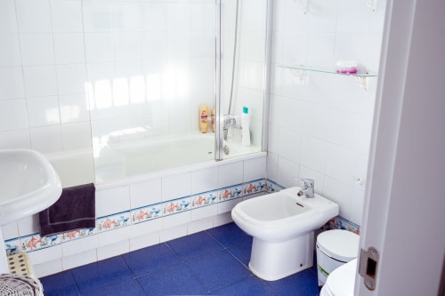 Baño luminoso en Guest Homes Málaga con azulejos blancos, piso azul, bañera con panel de cristal, bidet y lavamanos