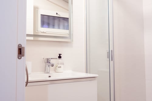Lavamanos moderno y espejo en Guest Homes Málaga con pantalla digital y cabina de ducha de cristal